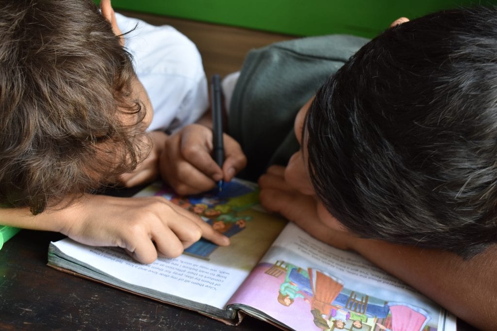 Two young kids reading, pointing to words in a book.