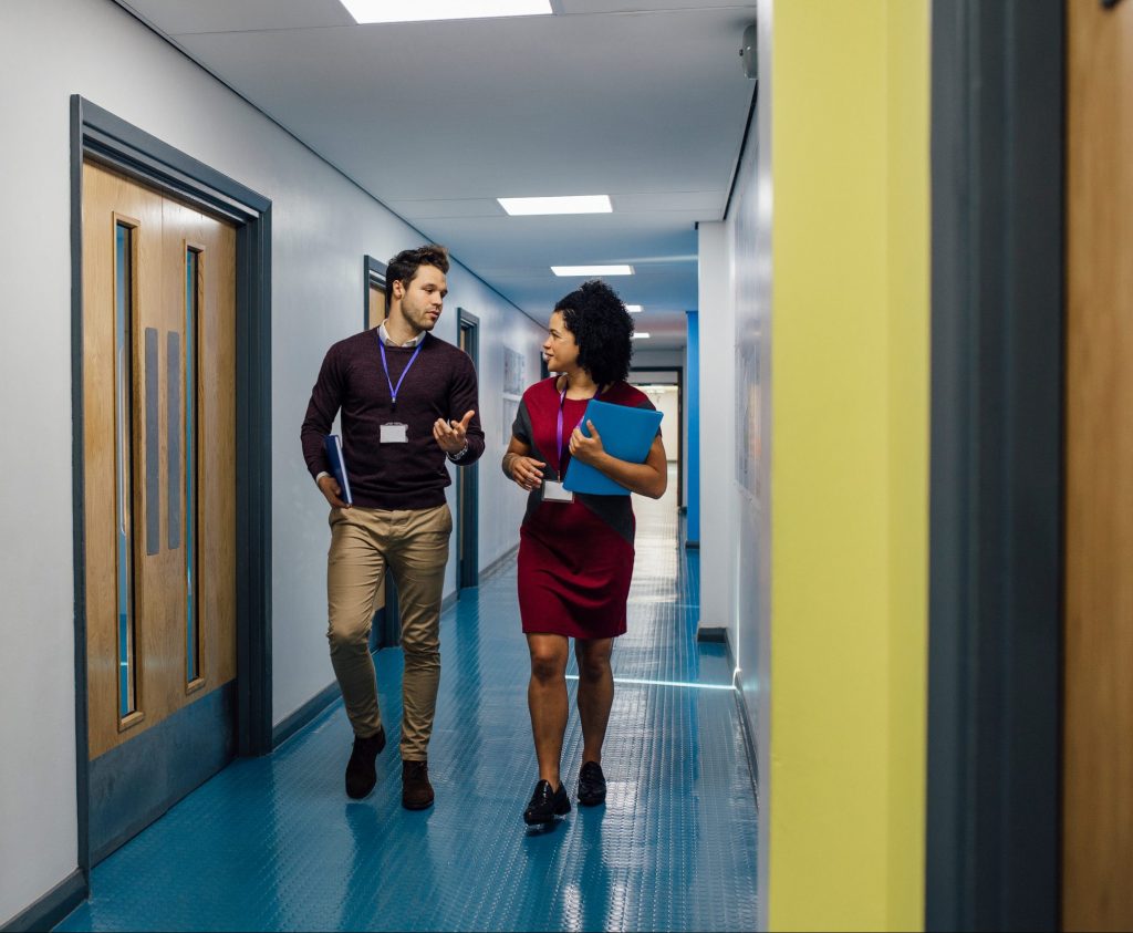 Two teachers are talking in the school hall as they walk to their next lesson together.